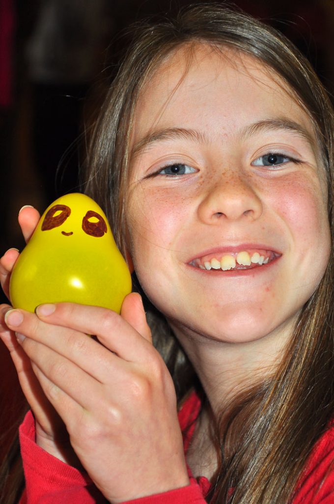 Close-up of a girl holding a yellow balloon filled with sand and painted with a face.